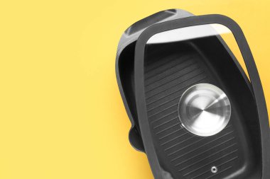 Sarı arka planda siyah tencere ve cam kapak, üst manzara. Metin için boşluk