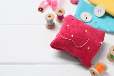 Beyaz ahşap masada iğneli kırmızı iğnelik ve diğer dikiş aletleri. Metin için boşluk