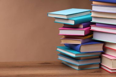 Açık kahverengi arkaplan ile ahşap masa üzerinde renkli kitap yığınları, metin için boşluk
