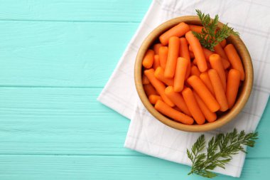 Açık mavi ahşap masa üzerinde bebek havuçları ve yeşil yapraklar, üst manzara. Metin için boşluk