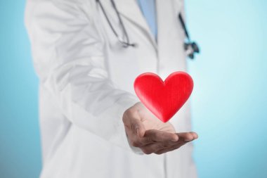 Açık mavi arka planda kırmızı kalbi tutan doktor, yakın plan.