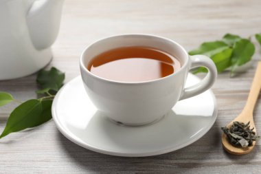 Yeşil çayı fincanda, kaşıkta ve yaprakları gri ahşap masada serinletiyor.