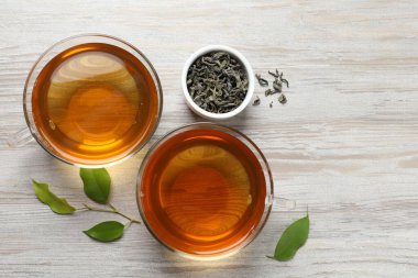 Yeşil çayı fincanlarda ve yaprakları açık ahşap masada serinletiyor.