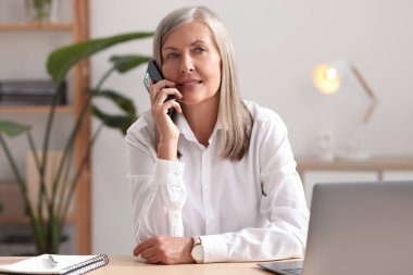 Evde cep telefonu kullanan yaşlı bir kadın.