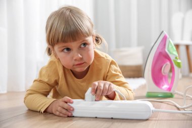 Little child playing with power strip and iron plug on floor indoors. Dangerous situation