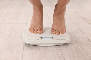 Woman standing on floor scales indoors, closeup