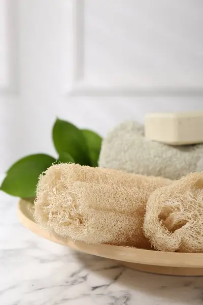 stock image Loofah sponges, soap, towel and green leaves on white marble table