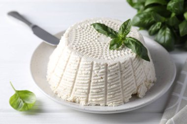 Lezzetli ricotta (krem peynir), beyaz ahşap masada bıçak ve fesleğen, yakın plan.