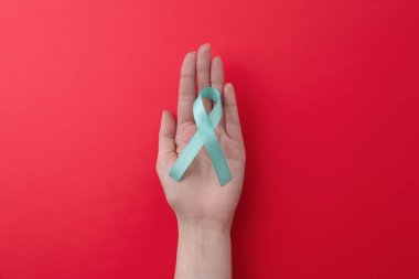 Woman holding turquoise awareness ribbon on red background, top view clipart