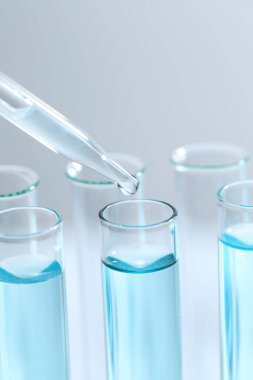 Işık arka planında pipetten test tüpüne sıvı damlatılıyor, yakın plan