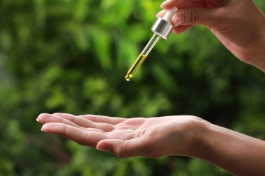 Woman dripping essential oil from pipette outdoors, closeup