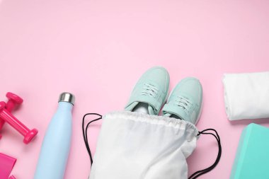 Beyaz çizgili çanta, spor ayakkabıları ve spor aletleri pembe arka planda, düz yatış. Metin için boşluk