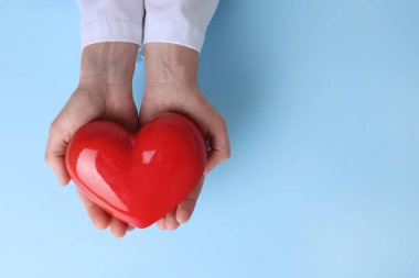 Doktor açık mavi arka planda kırmızı kalbi tutuyor. Metin için boşluk