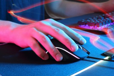 Gamer using modern wired computer mouse in neon lights at dark table, closeup clipart