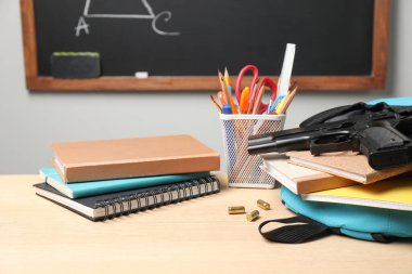 Silah, mermiler ve okul kâğıtları kapalı alandaki tahtanın yanındaki ahşap masada.