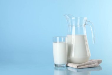 Açık mavi arka planda sürahi ve bir bardak taze süt, metin için boşluk