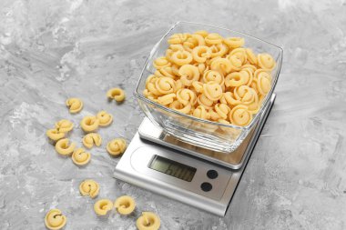 Mutfak terazisi ve gri desenli masada bir kase makarna.