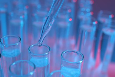 Renk arka planında pipetten test tüpüne sıvı damlatılıyor, yakın plan