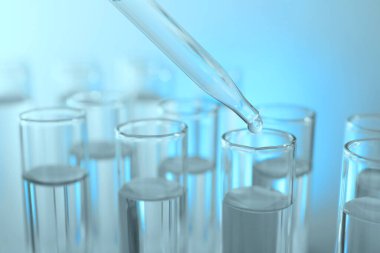 Işık arka planında pipetten test tüpüne sıvı damlatılıyor, yakın plan