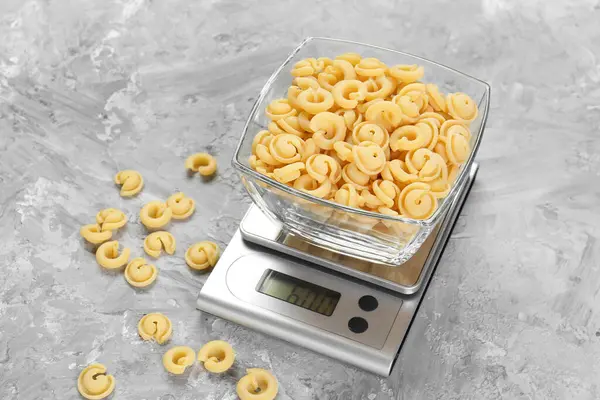 Mutfak terazisi ve gri desenli masada bir kase makarna.