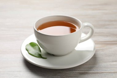 Yeşil çayı fincanda tazeleyen ve gri ahşap masada yaprak, yakın plan