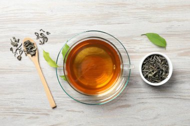 Fincanda yeşil çay, kaşık ve yapraklar hafif ahşap masa, düz uzanmış