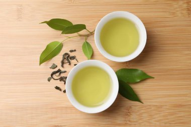 Yeşil çayı fincanda ve yaprakları tahta masada serinletiyor.