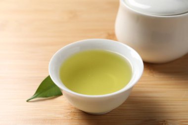 Yeşil çayı fincanda tazeleyen, şeker kasesi ve yaprak ahşap masada, yakın plan