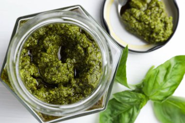 Kavanozda lezzetli pesto sosu ve beyaz masada fesleğen.
