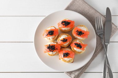 Delicious puff pastry with cream cheese, salmon, black caviar and cutlery on white wooden table, top view. Space for text clipart