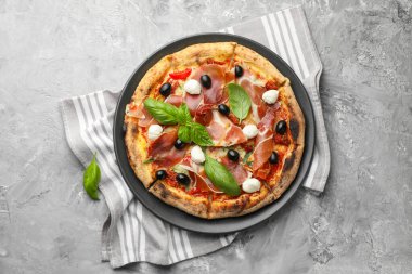 Tasty pizza with cured ham, olives, mozzarella cheese, sun-dried tomato and basil on gray textured table, top view