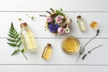 Aromaterapi. Farklı temel yağlar, yeşil dal ve beyaz ahşap masa üzerindeki çiçekler, düz uzanış