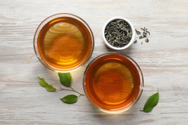 Yeşil çayı fincanlarda ve yaprakları açık ahşap masada serinletiyor.