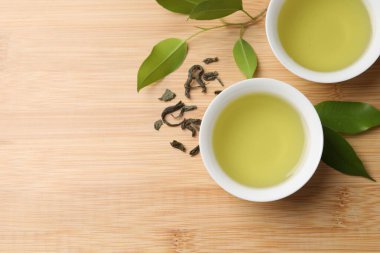 Yeşil çayı fincanlarda ve yaprakları ahşap masada, düz yerde serinletiyor. Metin için boşluk