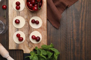 Process of making dumplings (varenyky) with cherries. Raw dough and ingredients on wooden table, flat lay. Space for text clipart