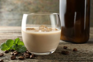 Coffee cream liqueur in glass, mint and beans on wooden table, closeup clipart