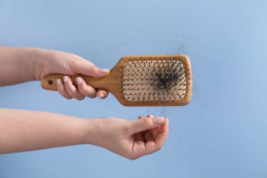 Woman taking her lost hair from brush on light blue background, closeup