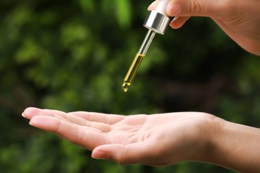 Woman dripping essential oil from pipette outdoors, closeup