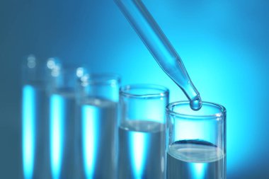 Işık arka planında pipetten test tüpüne sıvı damlatılıyor, yakın plan