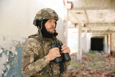 Military mission. Soldier in uniform with binoculars inside abandoned building