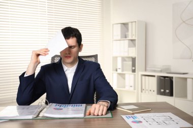 Embarrassed man with document at wooden table in office clipart