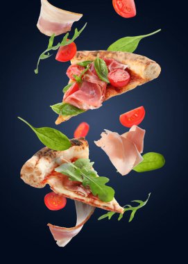 Lezzetli pizza dilimleri ve koyu mavi arka planda havadaki malzemeler.