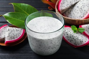 Lezzetli pitahaya smoothie ve siyah ahşap masada taze meyveler, yakın plan.