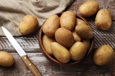 Bir sürü taze patates, kase ve bıçak tahta kırsal masada, düz yatıyordu.