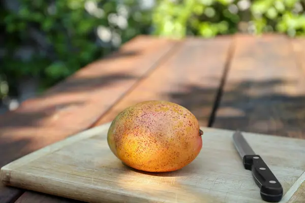 stock image Board with tasty mango and knife on wooden table outdoors