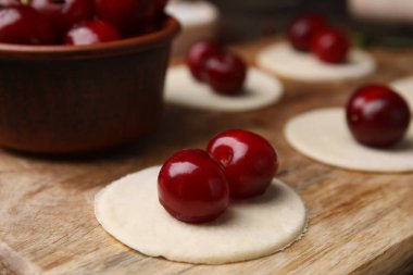 Process of making dumplings (varenyky) with cherries. Raw dough and ingredients on wooden table, closeup clipart