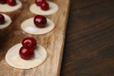 Process of making dumplings (varenyky) with cherries. Raw dough and ingredients on wooden table, closeup. Space for text clipart