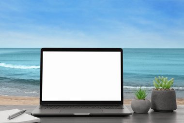 Kumsaldaki işyeri, uzak ofis. Kumlu deniz kıyısında dizüstü bilgisayarlı bir masa. Tasarım için model