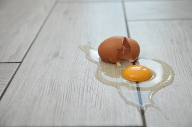 Açık gri ahşap zeminde kırılmış çiğ yumurta ve kabuk, kapalı alanda, yakın plan. Metin için boşluk