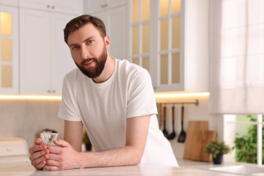 Sabahları mutfakta bir bardak su taşıyan genç bir adam.